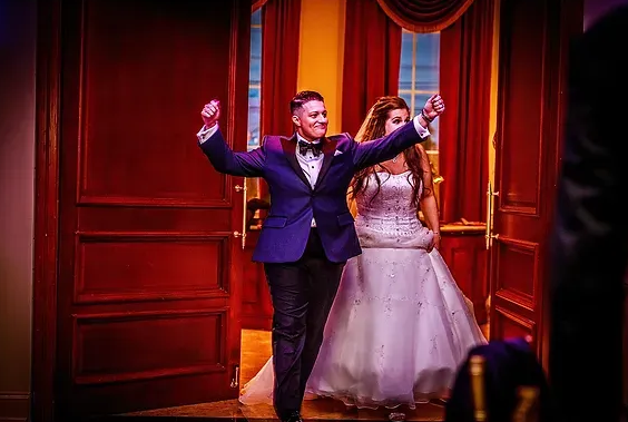 Two performers in formal attire dance on a theater stage with red curtains and warm lighting
