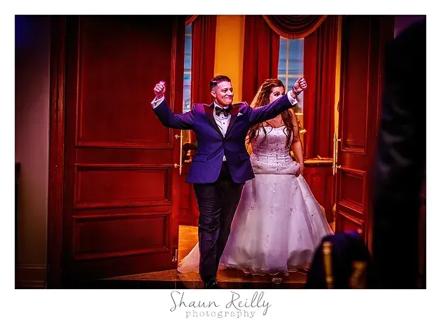 Bride and groom dancing joyfully in a warmly lit doorway with red curtains and wood paneling