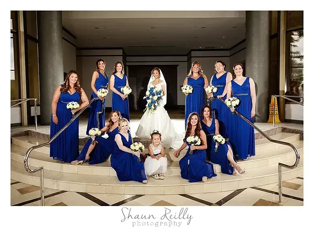 Bridal party in blue dresses poses around bride in white gown in a hotel lobby