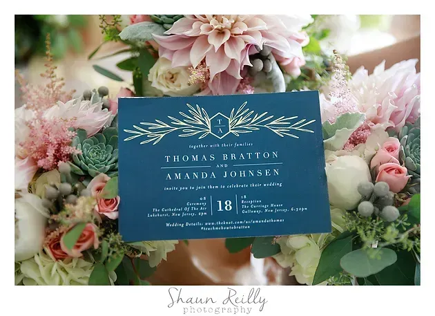Blue wedding invitation card among pastel pink flowers and greenery