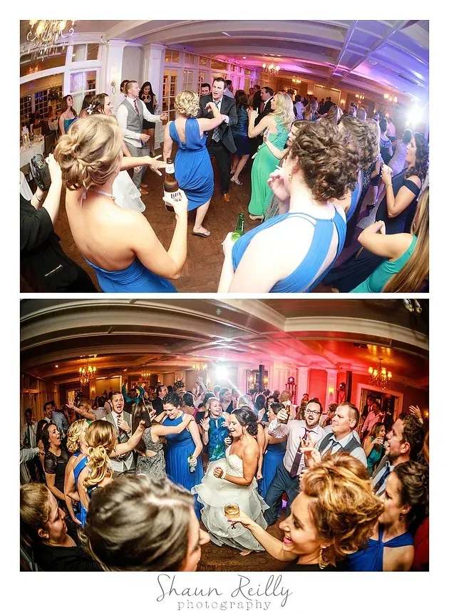 Crowded indoor party with guests dancing, clapping, and taking photos under warm colorful lights.