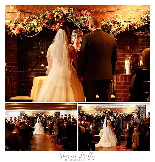 Wedding ceremony by a brick fireplace, with bride and groom facing officiant under a floral arch.