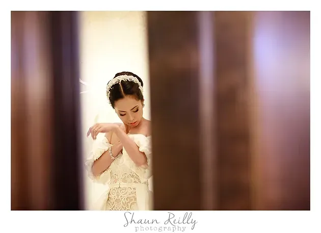 Bride in a white dress adjusting her bracelet, framed by a soft-focus doorway.