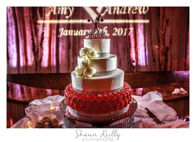 Three-tier white and red wedding cake on a table with “Amy & Andrew January 16, 2017” backdrop