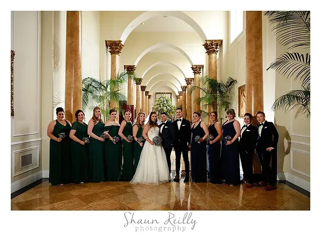Wedding party posing in a grand arched hallway with bridesmaids, groomsmen, bride, and groom