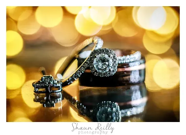 Wedding rings on a reflective surface with warm golden bokeh lights in the background