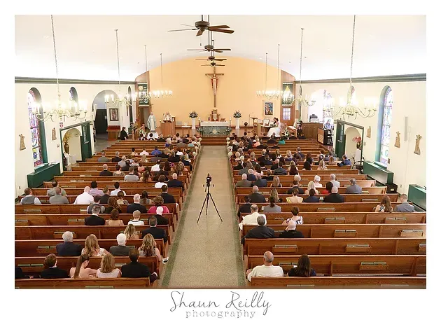 Wide view of church sanctuary with congregation seated in wooden pews facing the altar and crucifix