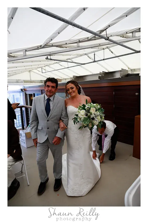 Bride and groom walking together at a wedding under a white canopy, both smiling
