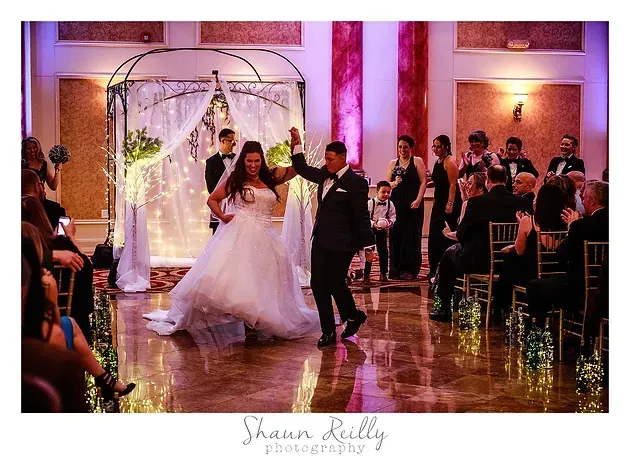 Bride and groom dance in a decorated wedding hall with guests watching