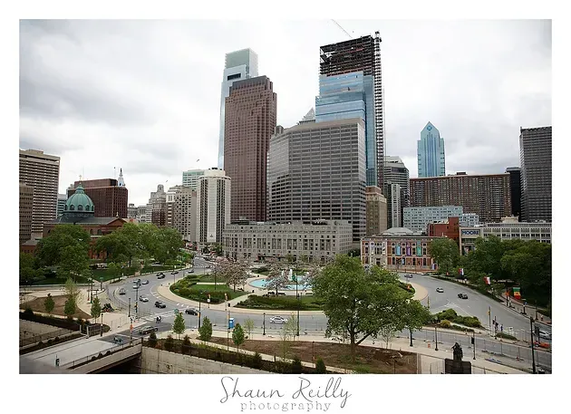 City skyline with tall buildings and a plaza fountain under cloudy skies