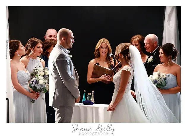 Wedding ceremony with bride and groom facing each other, wedding party standing behind them on stage