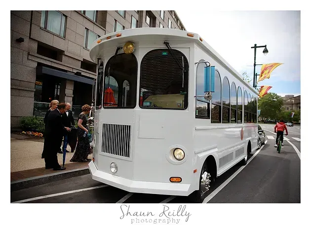 White trolley bus on a city street with pedestrians and storefronts nearby