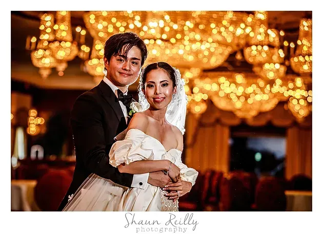 Couple posing in formal wear beneath warm chandelier lights at a wedding reception