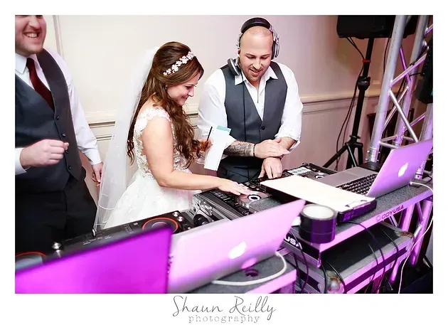 Bride and DJ mixing music at a wedding reception, lit by purple stage lights