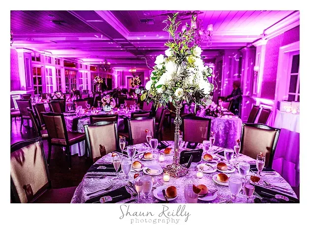 Elegant banquet hall with purple lighting, round tables set for a formal event, and a decorated center arrangement