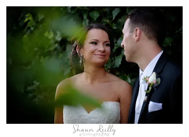 Bride and groom smiling at each other in a lush outdoor wedding portrait.