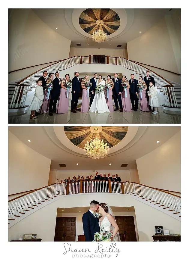 Wedding party posed on a grand staircase beneath a chandelier in a bright ballroom