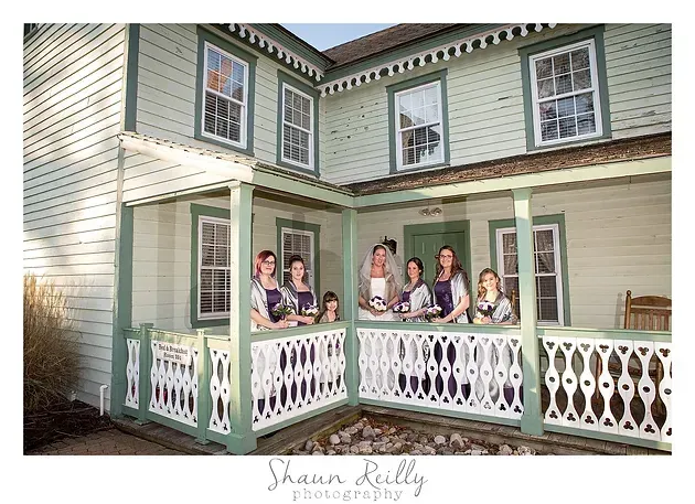 People standing on a porch of a light green house, leaning on white railings.
