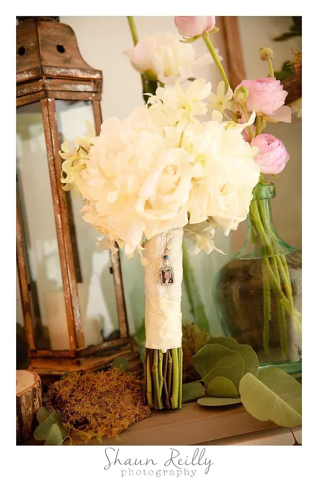 White and pale pink floral bouquet beside a rustic lantern and glass bottle on a textured surface