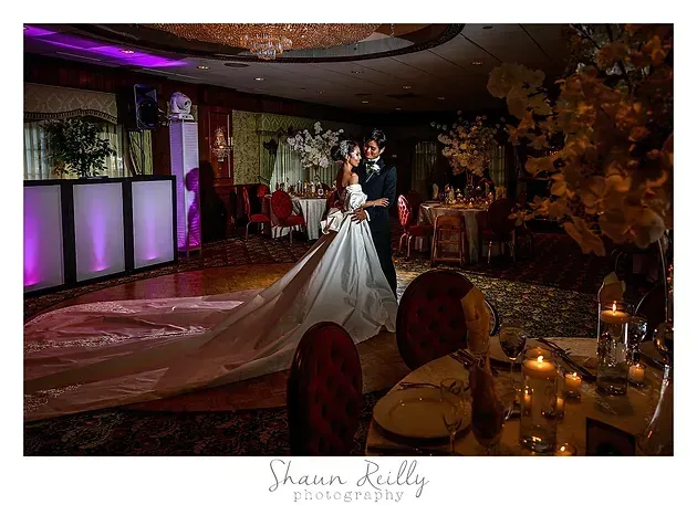 Bride and groom on a lit stage at a wedding reception, with candlelit tables in the foreground
