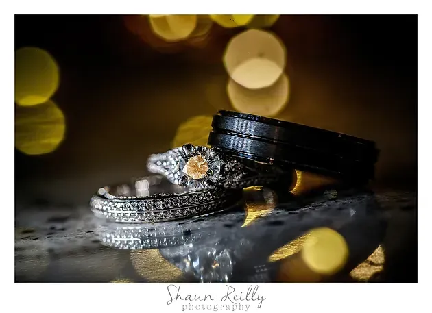 Two diamond wedding rings on a reflective surface with warm golden bokeh lights in the background