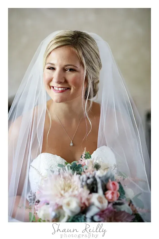 Smiling bride in a white veil holding a pastel bouquet indoors