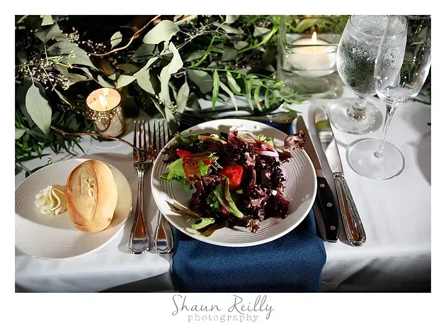 Elegant candlelit table setting with salad, bread, wine glasses, and greenery