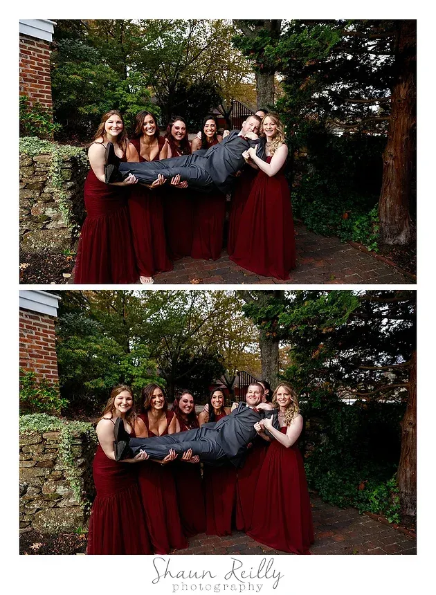 Bridesmaids in burgundy dresses carry a groom in black suit outdoors under autumn trees.