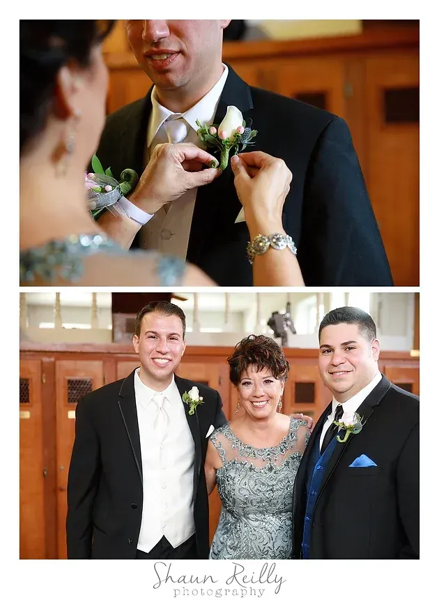 Wedding guests pinning a white boutonniere on a groom, with a smiling couple posing below.