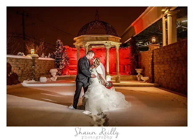Bride and groom pose in a snowy courtyard lit by warm red lights at night