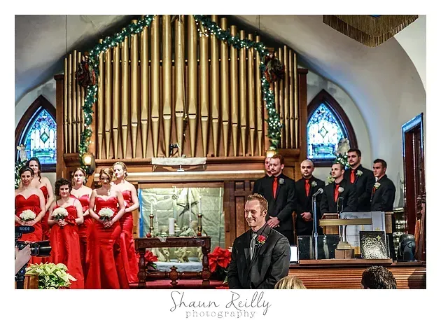 Wedding party in a church, with bridesmaids in red and groomsmen in dark suits before the organ