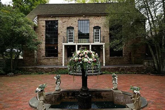 Brick house with tall windows and a central fountain and flower arrangement in a brick courtyard