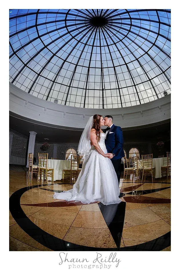 Bride and groom embracing in a grand glass-domed atrium, wedding reception setting