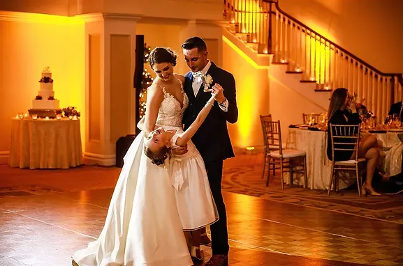 Bride and groom dancing in a warmly lit reception hall with a wedding cake in the background