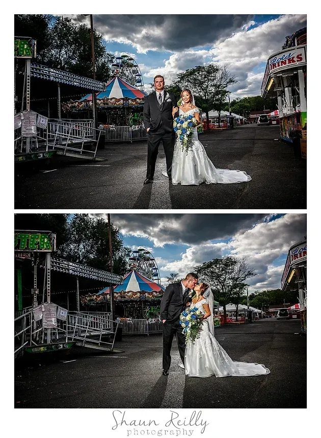 Bride and groom posing outdoors at a fairground, with a white wedding gown and dark suit under dramatic clouds