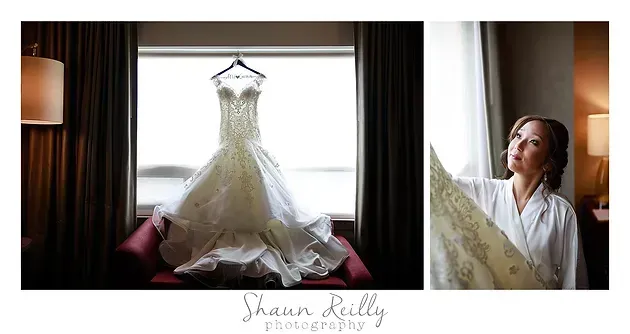 Wedding dress hanging by a bright window, with a woman smiling beside it in a dimly lit room