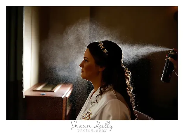 Woman in profile getting hair sprayed in a dimly lit room near a window