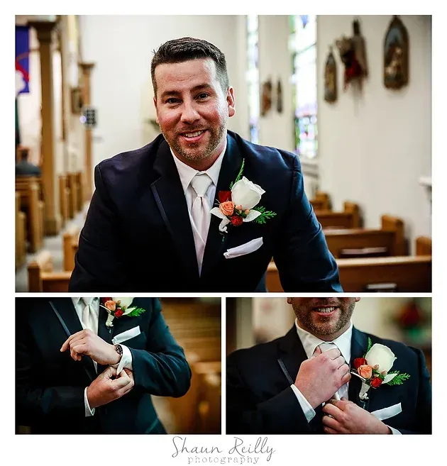 Smiling groom in navy suit adjusting boutonniere inside a church during wedding portraits