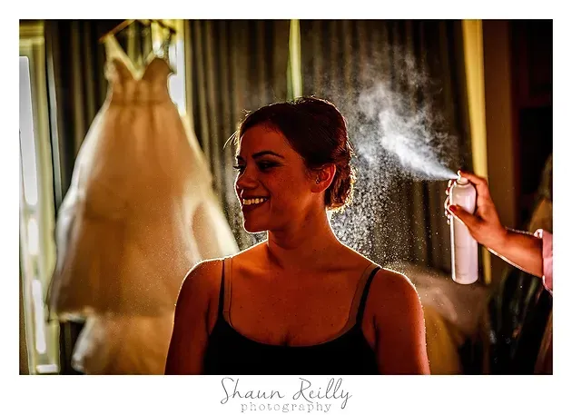 Woman smiles while getting a spray tan, with a dress hanging in the background.