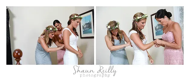 Three women in pastel dresses adjusting a bride’s white gown in a bedroom, with a decorative sign above.
