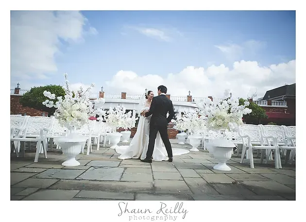 Bride and groom embrace at an outdoor wedding altar, framed by white chairs and floral arrangements.