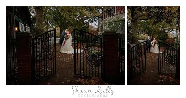 Bride in white dress standing by open black gates in a tree-lined garden path
