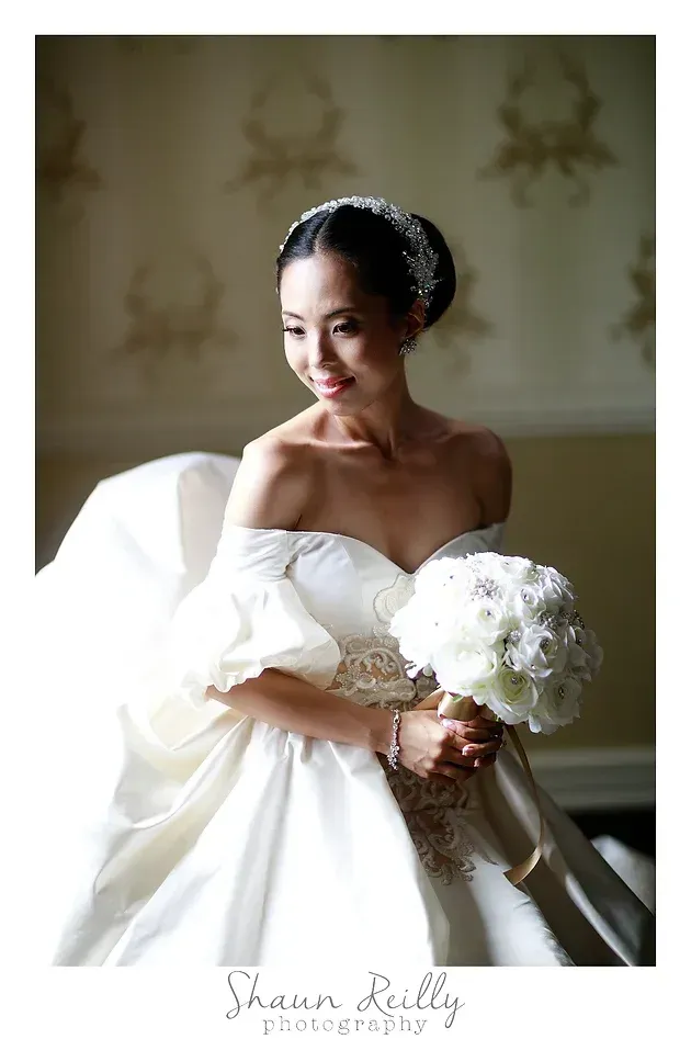 Bride in a white gown holding a bouquet, smiling softly in a bright bridal portrait.