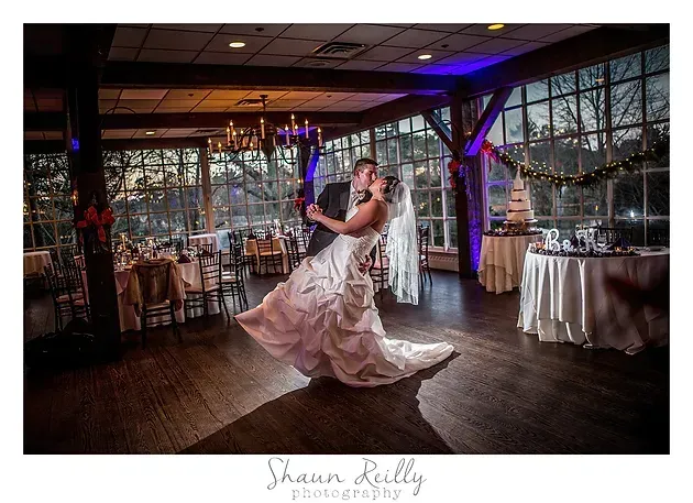 Bride and groom dancing in a decorated reception hall with purple lighting and tables set nearby
