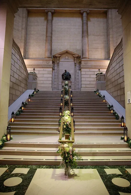 Grand staircase with floral garland and a statue at the top in a grand hall