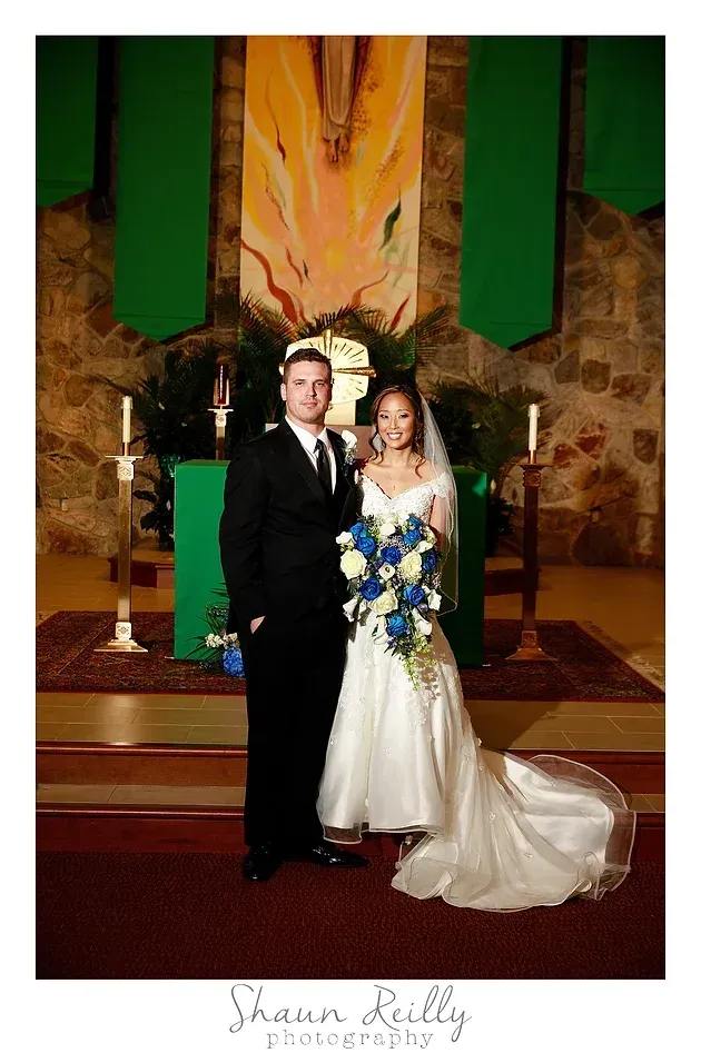 Bride and groom posing in a church, with green drapes and a floral altar backdrop