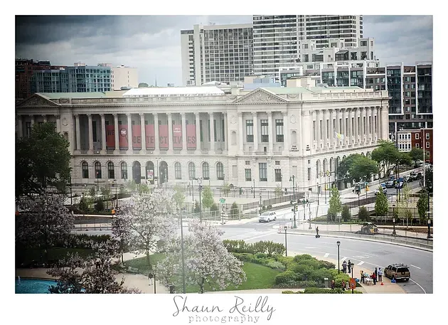 Large neoclassical civic building beside a busy intersection, with modern buildings in the background