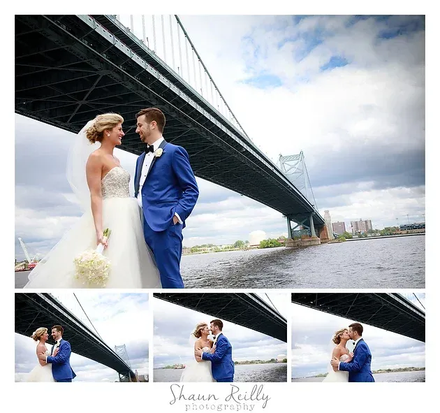 Bride and groom in wedding attire pose under a bridge by the water.