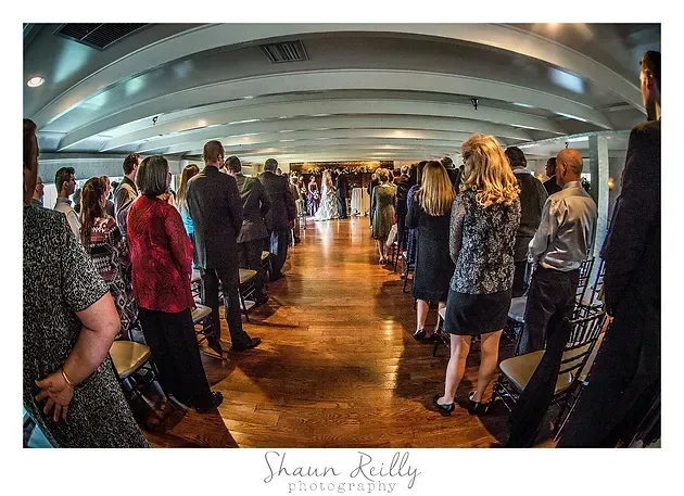 People standing in a curved indoor walkway, with warm light reflecting on the wooden floor.
