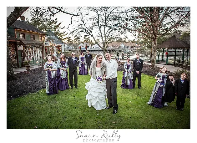 Wedding party posing outdoors in a garden, with bride and groom centered among attendants in purple dresses and gray suits